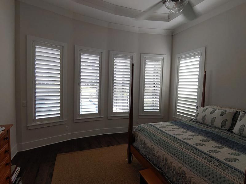 Bedroom with custom white shutters behind a four-poster bed