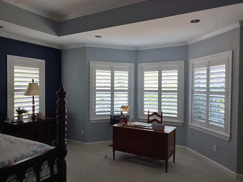 White plantation shutters on the corner windows of a bedroom office