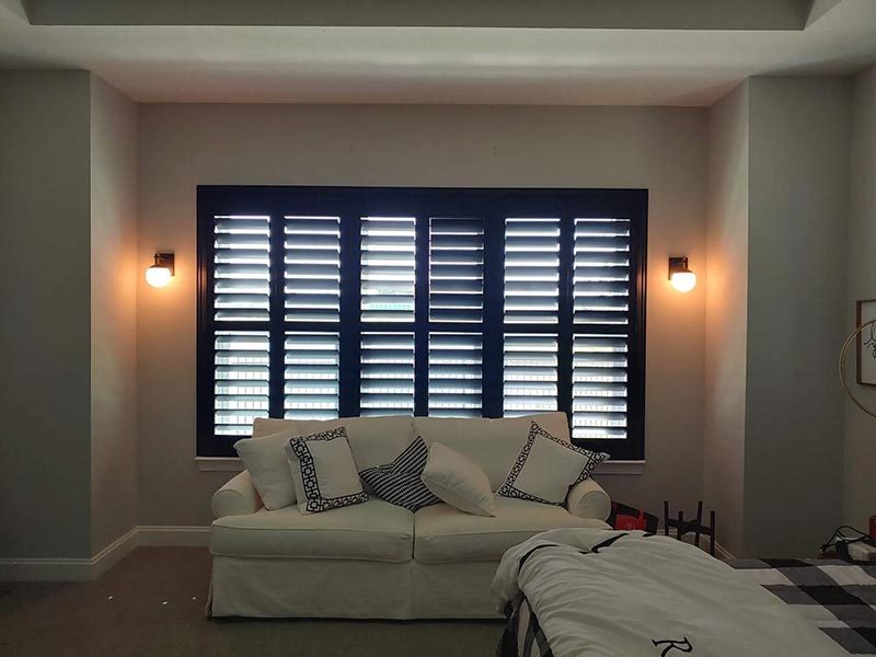 Black plantation shutters above a sitting area lit by wall sconces