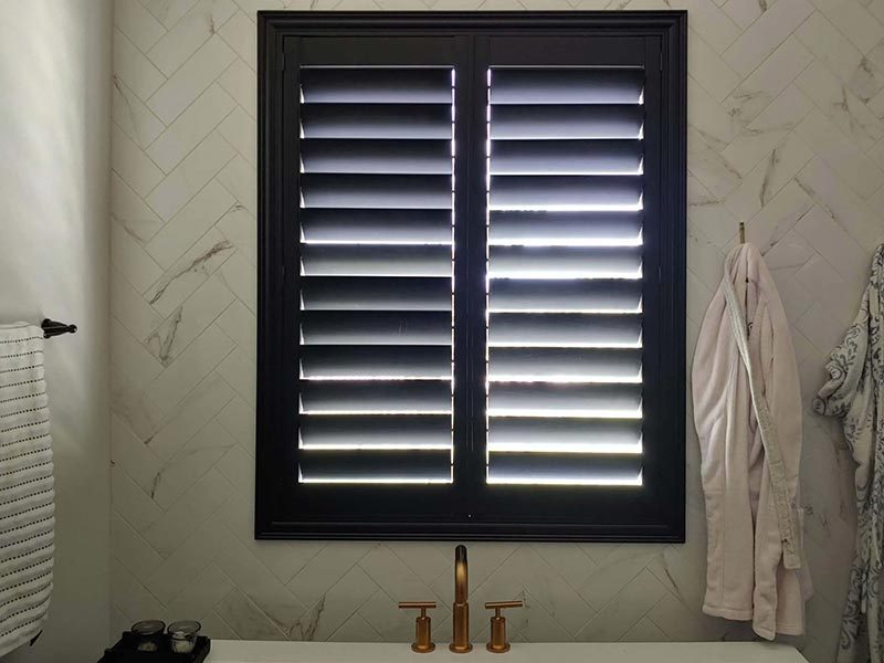 Black plantation shutter over a marble herringbone bath wall