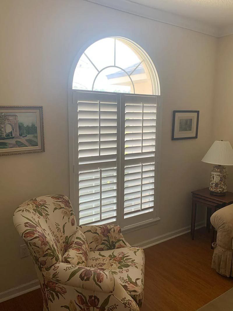 Arch-top shutter beside a reading chair in a classic room
