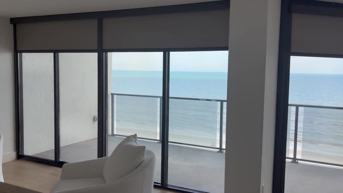 Motorized shades running across an oceanfront wall of glass