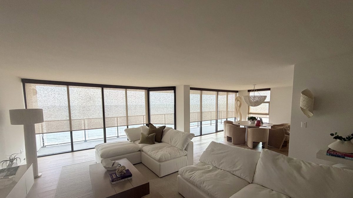Roller shades lowered across an oceanfront living room wall of glass