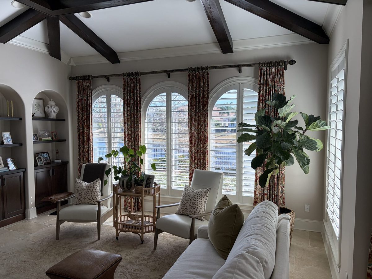 Arched plantation shutters framed by drapery in a beamed living room